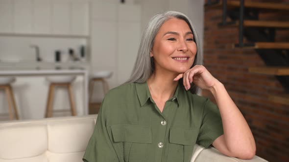 Lighthearted Positive Middleaged Woman with Long Gray Hair Sitting on Sofa