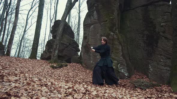 Man in Traditional Japanese Clothes, with a Sword, a Katana, Trains Martial Arts in the Forest alt
