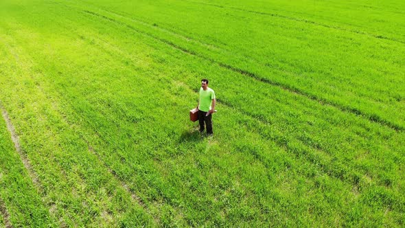 Sad Confused Man Alone Standing in a Green Field, Holding Suitcase in a Hand, Aerial Shot From Drone