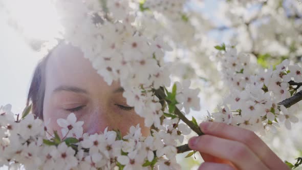 Man Smells Pleasant Aroma of White Flowers on Tree Branch alt