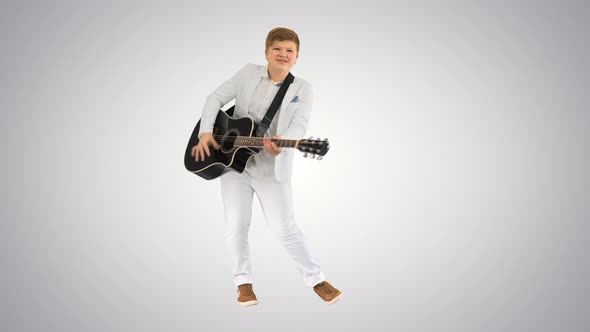 Boy in White Playing Acoustic Guitar and Dancing on Gradient Background. alt
