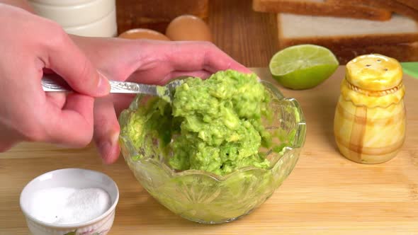 Hands mashing avocado with fork in a bowl, male chef hands preparing guacamole recipe. Cooking alt