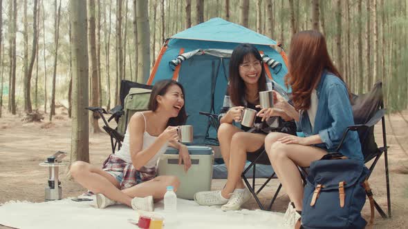 Group of young asia camper friends sitting in chairs by tent in forest.