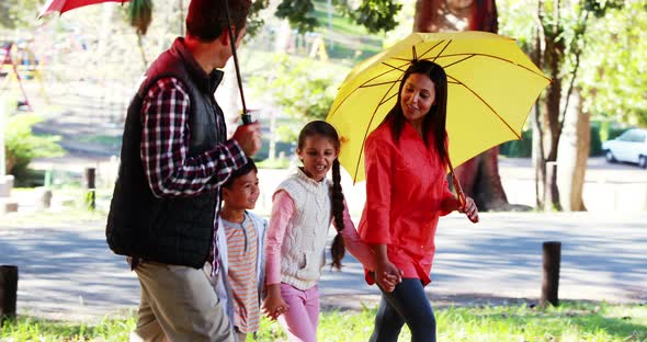 Family walking together in park with umbrella alt