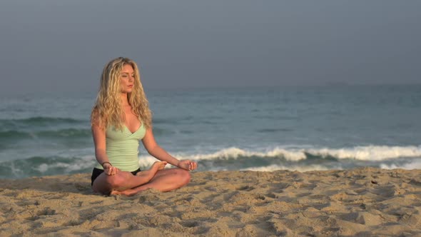 A young woman doing yoga on the beach while sitting. alt