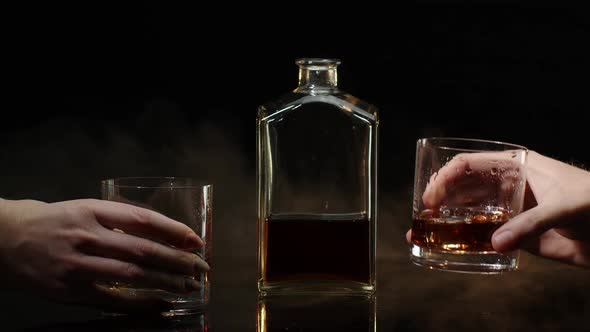 Two Hands with Glasses of Cognac Whiskey with Ice Cubes Making Cheers Toast on Black Background alt
