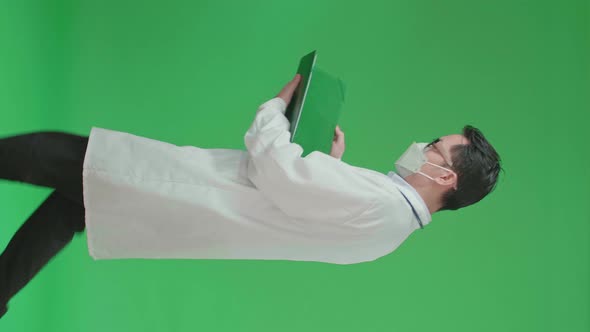 Asian Doctor With Stethoscope Wearing Mask, Opening Document File While Walking On Green Screen alt