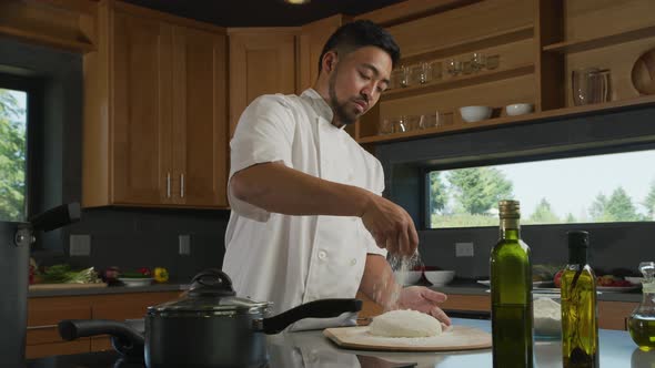 Chef in kitchen sprinkling flour onto dough