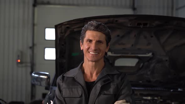Zoom out camera view of the calm confident senior auto mechanic wearing gloves alt