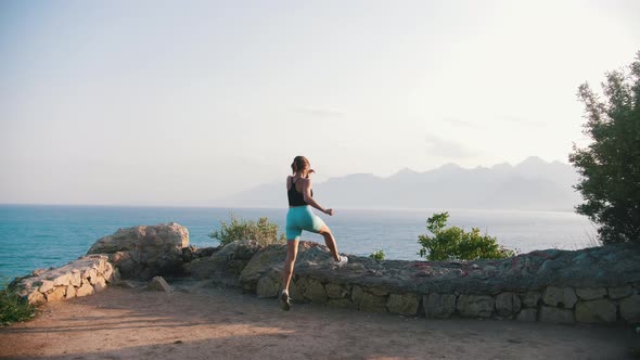 Young Woman in Sports Clothes Running to the Rocky Fence on the Hill By the Sea alt