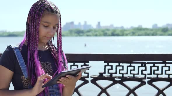 Young Girl Uses a Tablet Standing By the River alt