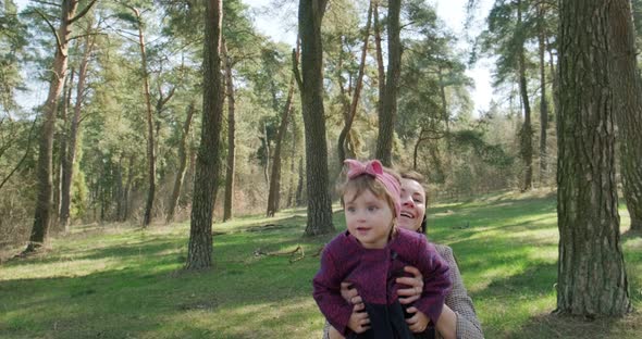 Happy Little Girl Walking and Playing with Mother Among Trees in Coniferous Forest. Healthy Child alt