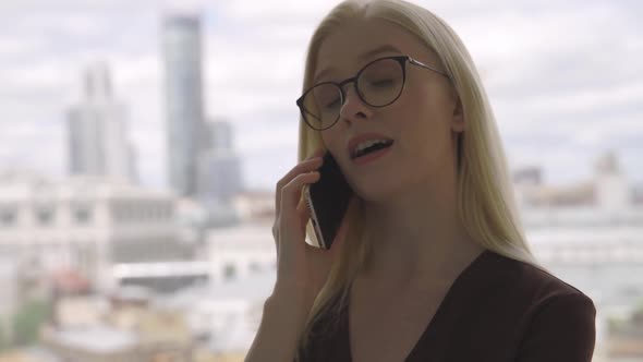 Confident Business Woman with Glasses Talking on the Phone with Her Business Partner Near a Large