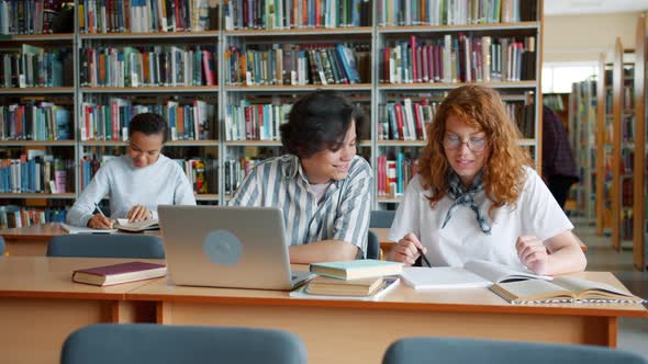 Students Studying in Library Talking Using Laptop Doing Research Together alt
