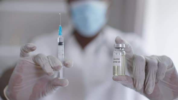 Closeup Syringe and Ampoule with Coronavirus Vax in Male African American Hands in Gloves alt
