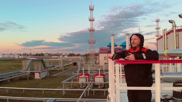 Oil and Gas Industry Bearded Engineer in a Protective Hood Transmitting Readings on a Walkietalkie