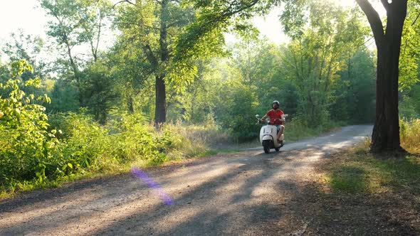 Happy Bearded Hipster Riding a Vintage Scooter in the Forest Road, Slow Motion. Handsome Man Rides alt