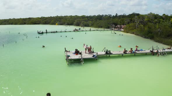Fly Over Wooden Piers at Lake Shore with People Enjoying Hot Sunny Day alt