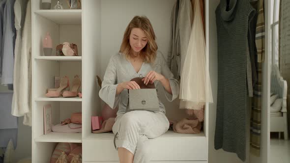 Stylish Young Mother Show Perfume to Curious Daughter Sitting on Wardrobe Shelve with Clothes alt