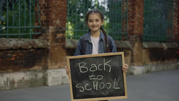 Portrait of Little Girl Standing Turn Around Smilling and Holding Schoolboard with Text Back to alt