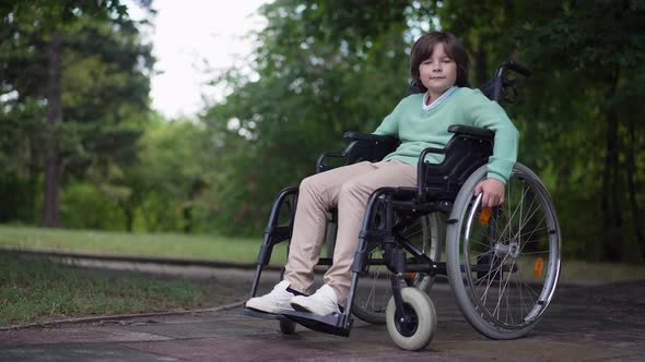 Wide Shot Happy Confident Disabled Boy in Wheelchair Looking at Camera Smiling alt