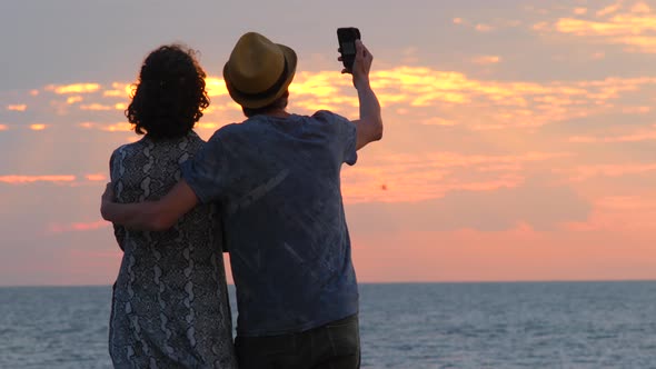 Beautiful young couple looking out for sunrise sunset, making selfie on smartphone