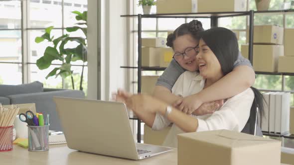 An Asian daughter hugs her mother while she is working from home. Postal parcel packaging box