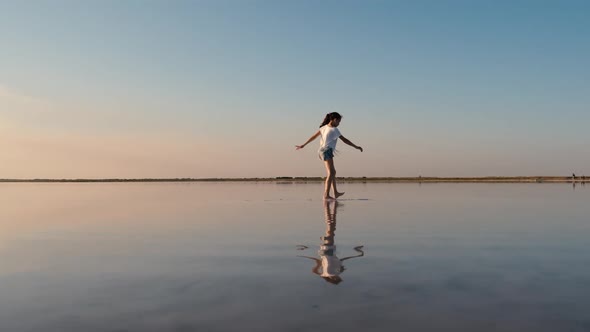 Teenage Traveler Girl Walking on a Salt Lake Reflecting the Sky alt