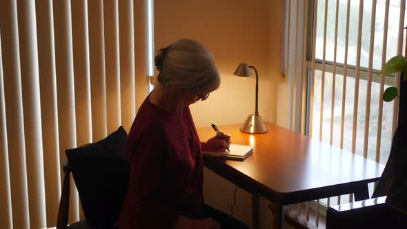 Middle aged caucasian woman with aging hands writing an old fashioned paper and pen mail letter or h alt