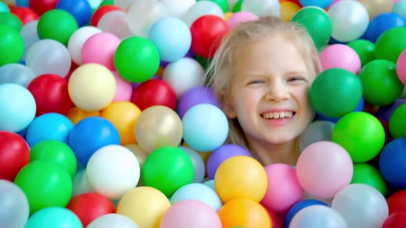 Cute Blonde Little Girl Lying on Multi Coloured Plastic Balls in Big Dry Paddling Pool in Playing alt