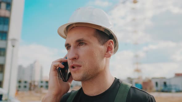 A Builder Wearing Helmet Is Talking By Phone While Inspecting Building Site alt