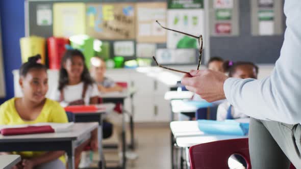 Midsection of diverse male teacher conducting lesson in classroom with children alt
