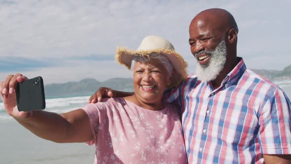 Mixed race senior couple taking a selfie with a smartphone at the beach alt