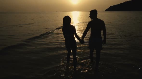 Silhouette of romantic couple lover holding hands while walking at the beach in sunset