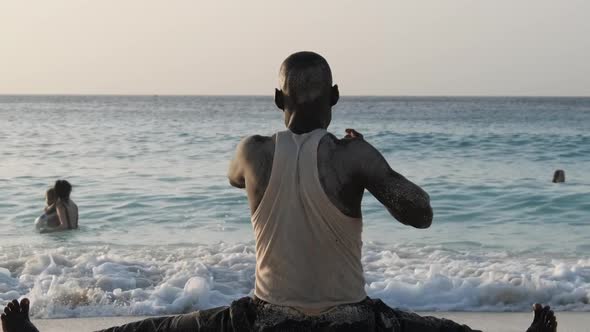 Athletic African Man Sits on Twine and Goes in for Sports on the Beach By Ocean alt