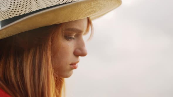 Close Up of Thoughtful Sad Redhead Girl in Straw Hat Standing Outside Outdoors in Nature Looking