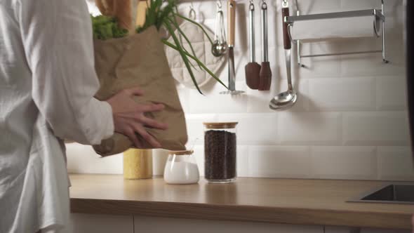 Woman Puts Eco Friendly Paper Bag With Fresh Vegetables, Baguette On Table In Modern Kitchen alt