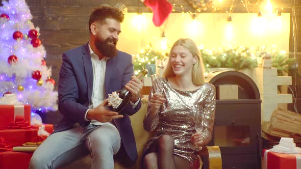 Happy New Year. Man Opening Bottle of Champagne Near Xmas Tree at Home. Young Loving Couple Enjoying alt