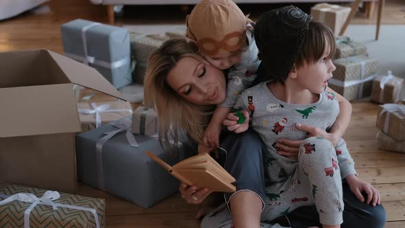 Young Family with Two Small Children Indoors with New Year's Decorations Reading a Book at Christmas alt