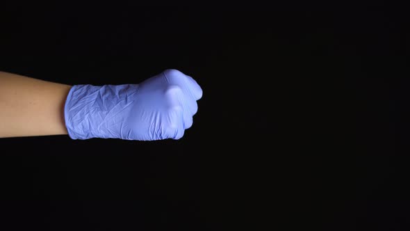 Female Hand in a Latex Medical Glove Makes an Fist Gesture Isolated on Black Background alt