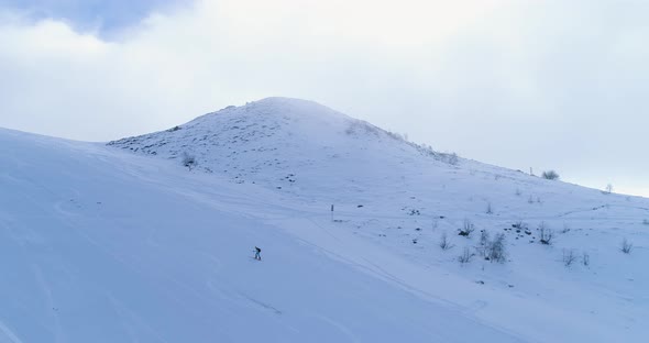 Side Aerial Over Winter Snowy Mountain Ski Track Field with Mountaineering Skier People Walking Up