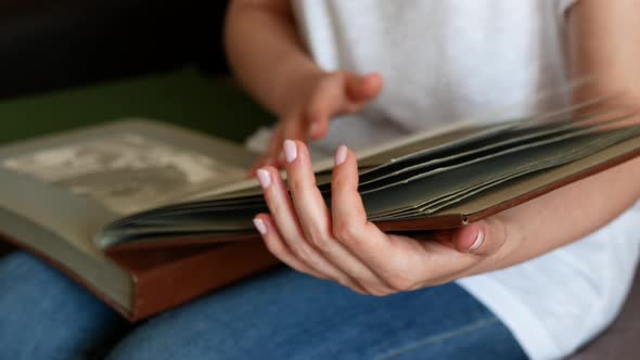 Woman is looking at black and white photos on the pages of her family photograph album