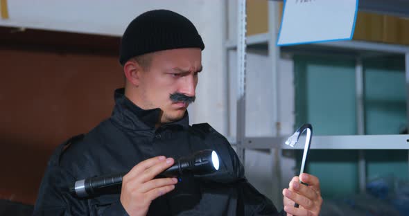 Suspicious Man with a Thick Mustache and in Black Uniform with Knitted Hat Looks at Crowbar with alt