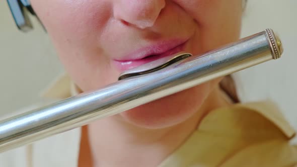 A woman lips with a flute is playing at home on the sofa in the living room, close-up