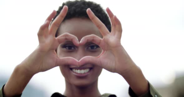 African Teenager Smiles with White Teeth Puts Hands in Front of Her Shows Fingers Heart Shape Sign alt