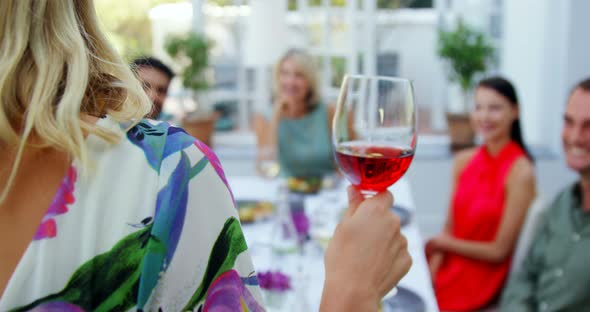 Friends applauding woman while having glass of wine alt