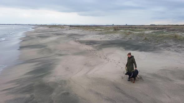 A Girl Walks with a Rottweiler Dog on a Leash Along the Beach in Cold Weather alt
