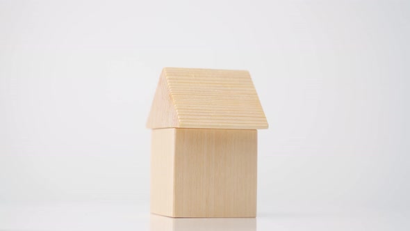 A toy house made of a wooden cube and a triangle in the form of a roof rotates on a white background alt