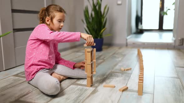 Happy Little Girl Play Game with Wooden Tower Blocks Bricks Sitting on the Floor at Home