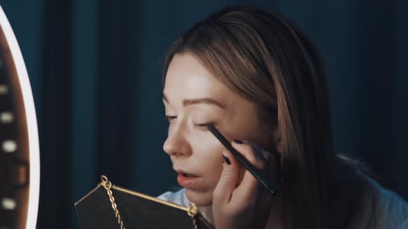 Woman Beauty Vlogger Uses Eyeliner Holding Mirror in Hand in Front of Ring Light